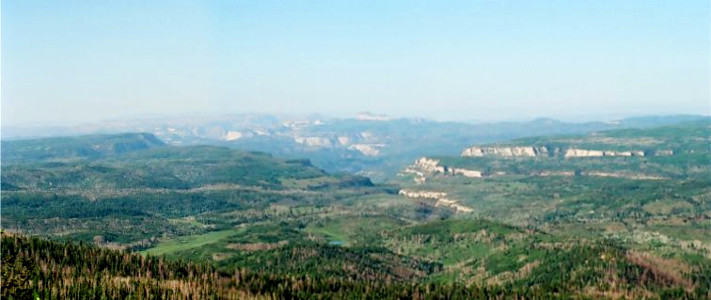 [Two photos stitched together displaying miles of tree-topped canyons and a small lake.]